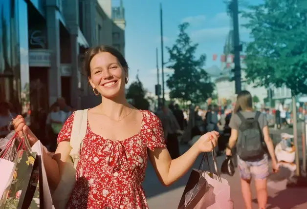 eine fröhliche junge Frau im roten Sommerkleid hat die Arme voller gefüllter Einkaufstaschen