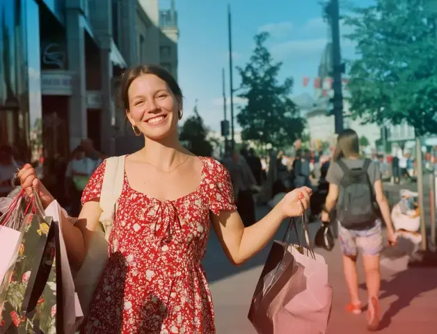 eine fröhliche junge Frau im roten Sommerkleid hat die Arme voller gefüllter Einkaufstaschen