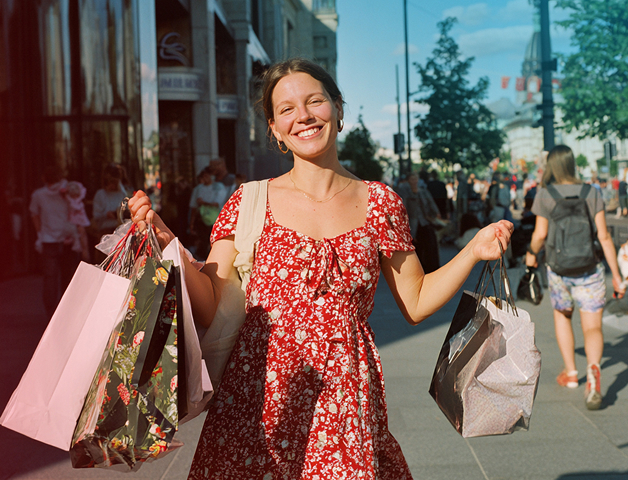 junge glückliche Frau im roten Sommerkleid trägt viele gefüllte Einkaufstaschen