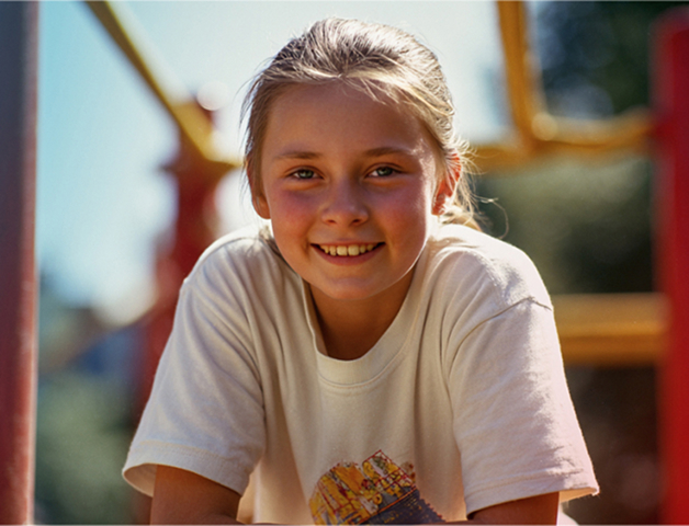 Mädchen im Grundschulalter sitzt auf einem Klettergerüst