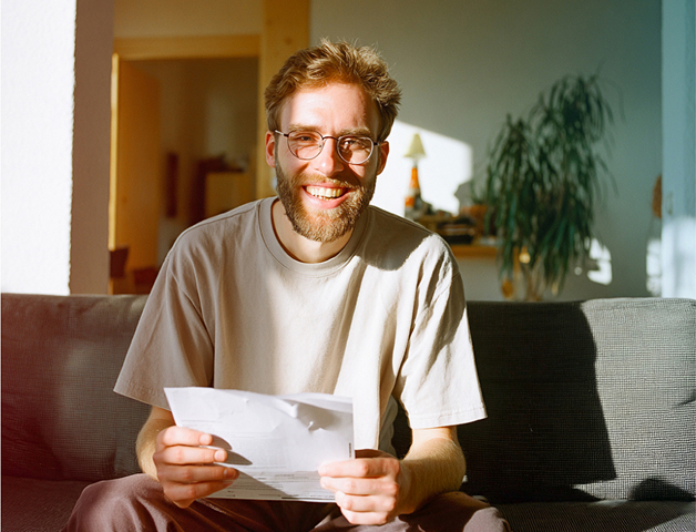 junger Mann mit Papieren in der Hand sitzt auf dem Sofa